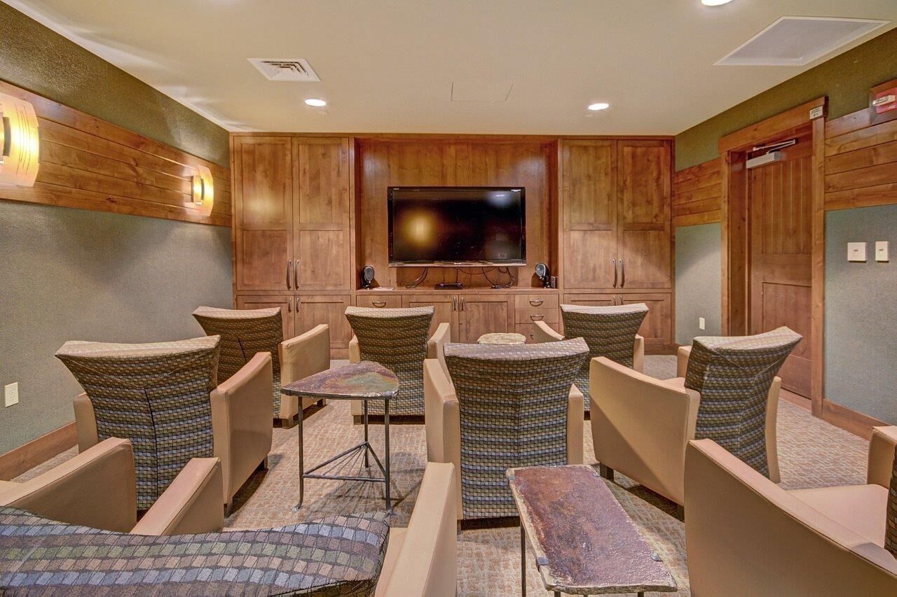 A room with a large flat-screen TV mounted on a wooden wall, surrounded by wicker chairs and a small table.