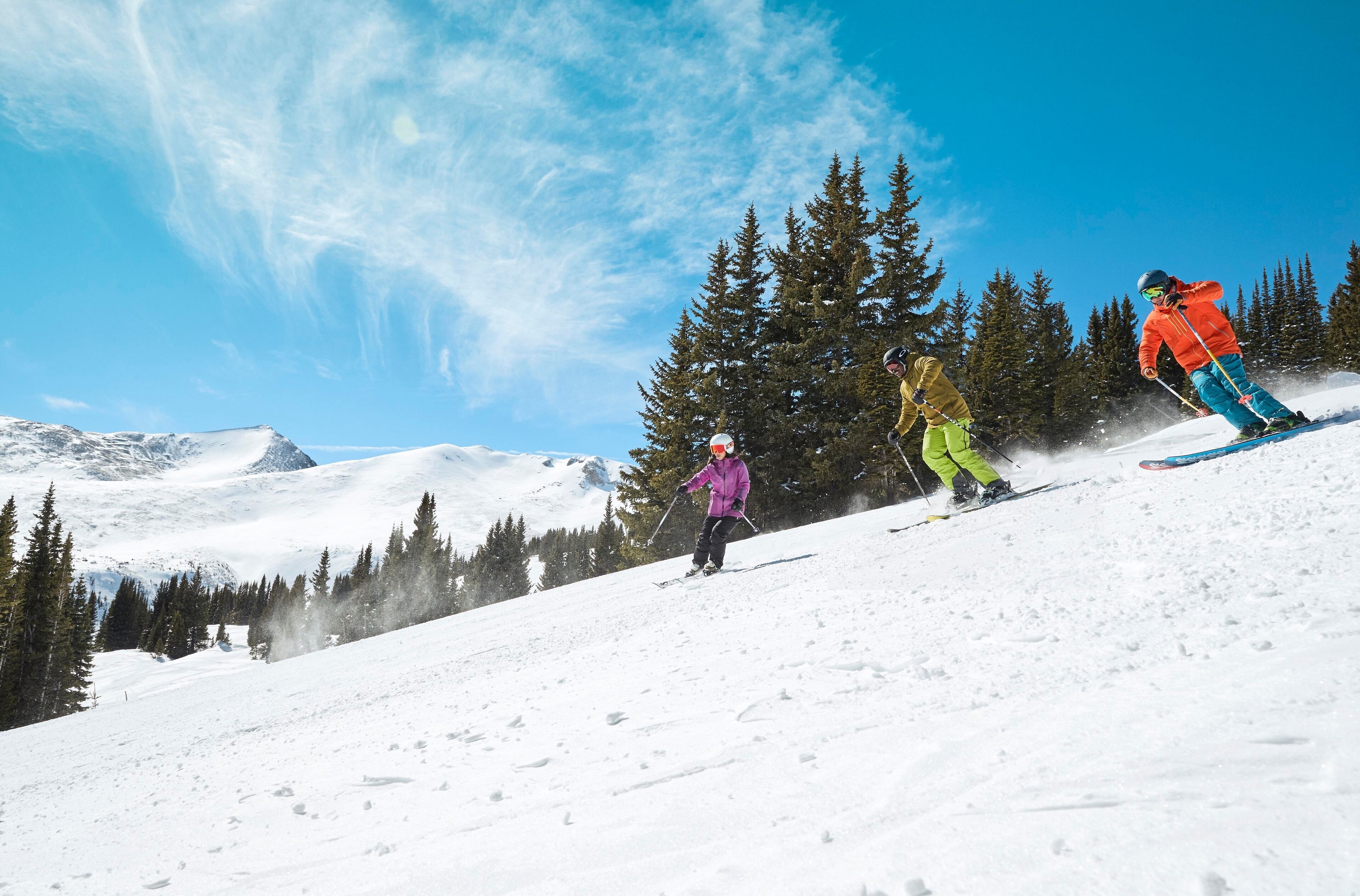 A snowy ski slope with trees and a clear blue sky.