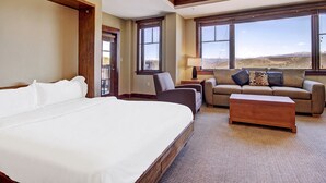 Ein Hotelzimmer mit einem großen Bett, einer Couch, einem Couchtisch und Blick auf Berge durch große Fenster.