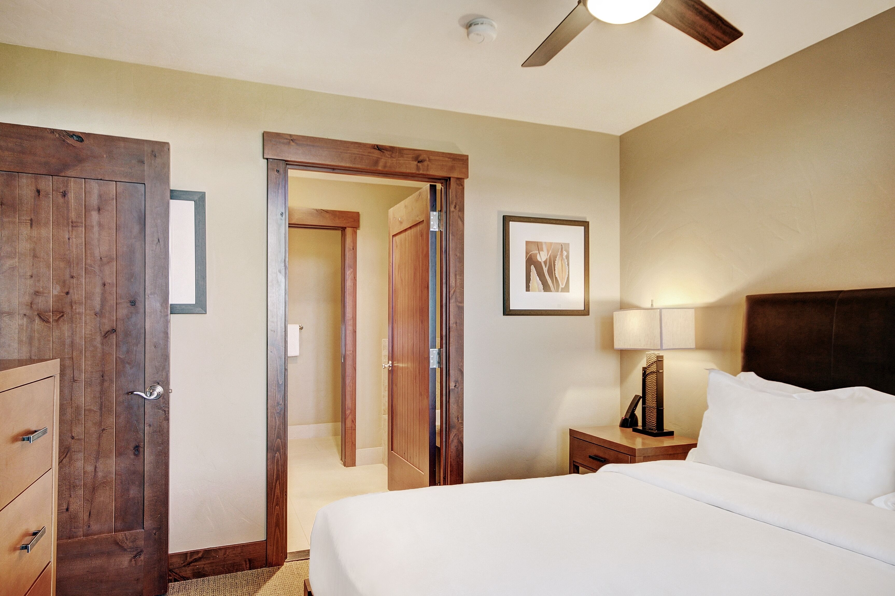 Une chambre d’hôtel avec un lit, une table de chevet, une lampe et une porte donnant sur une autre pièce.