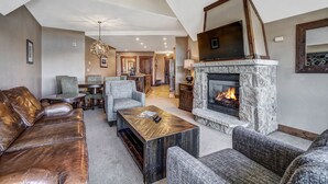 A spacious living room with a stone fireplace, leather sofa, and a dining area with a chandelier. - Premier 2br  At The Base Of Peak 7 2 Bedroom Condo by RedAwning (Breckenridge)