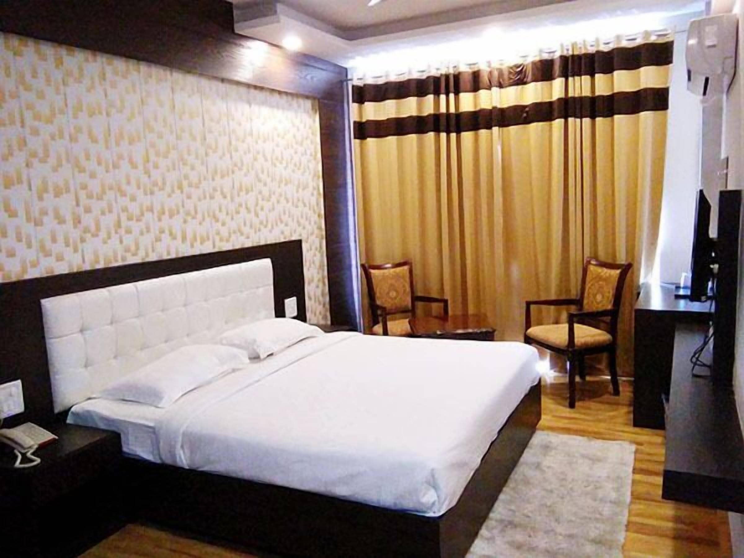 A hotel room with a large bed, two chairs, a desk, and a television.
