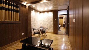 A hotel room with a wooden floor, a dining area with a round table and chairs, and a large window with curtains. - Paradise Ganga - A River Side Hotel (Rishikesh)