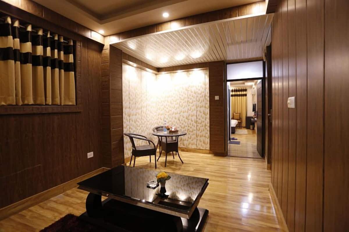A hotel room with a wooden floor, a dining area with a round table and chairs, and a large window with curtains.