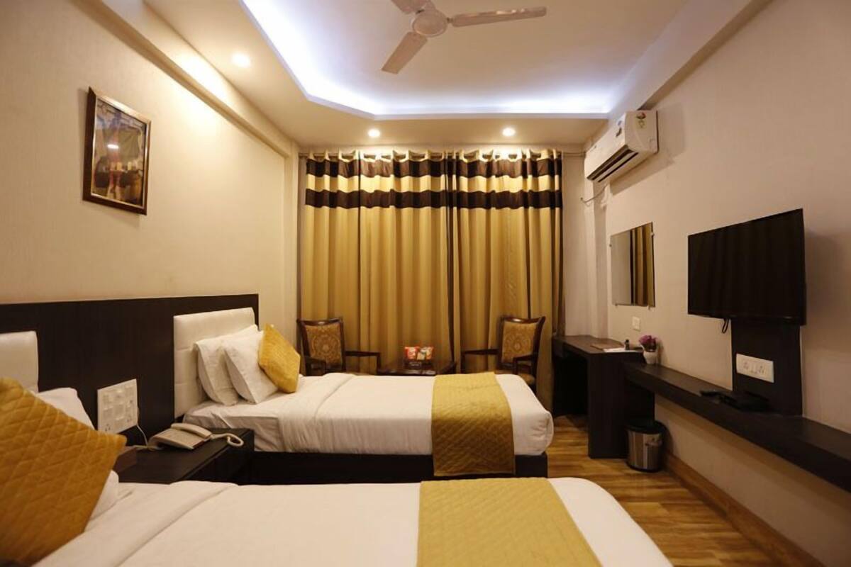 A hotel room with two beds, a desk, a chair, a TV, and an air conditioning unit.