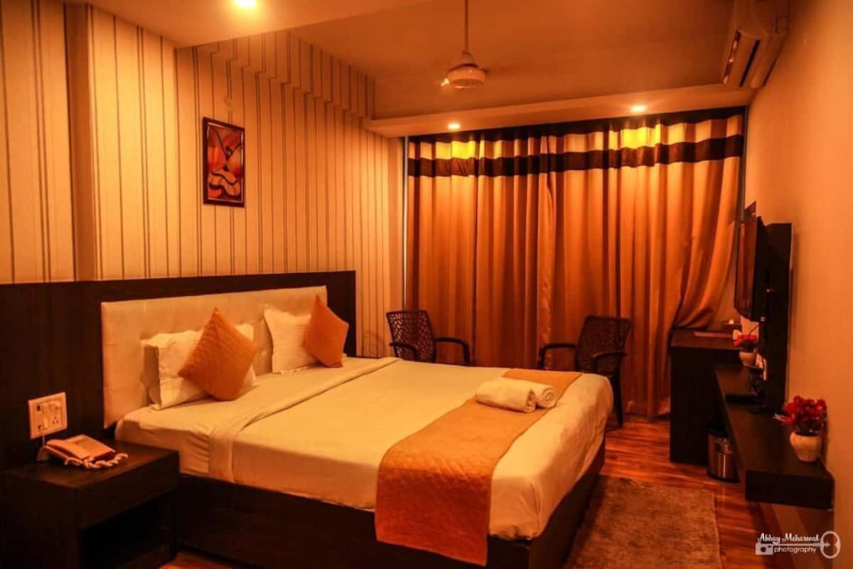 A hotel room with a large bed, a desk, a chair, and a television.