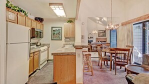 A modern kitchen with wooden cabinets, a central island, and a dining area with wooden chairs and a table.