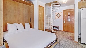 A bedroom with a large bed, wooden wardrobe, a white bench, and a spiral staircase.