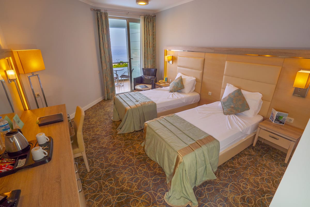 A hotel room with two beds, a desk with a coffee maker, and a view of the outdoors.