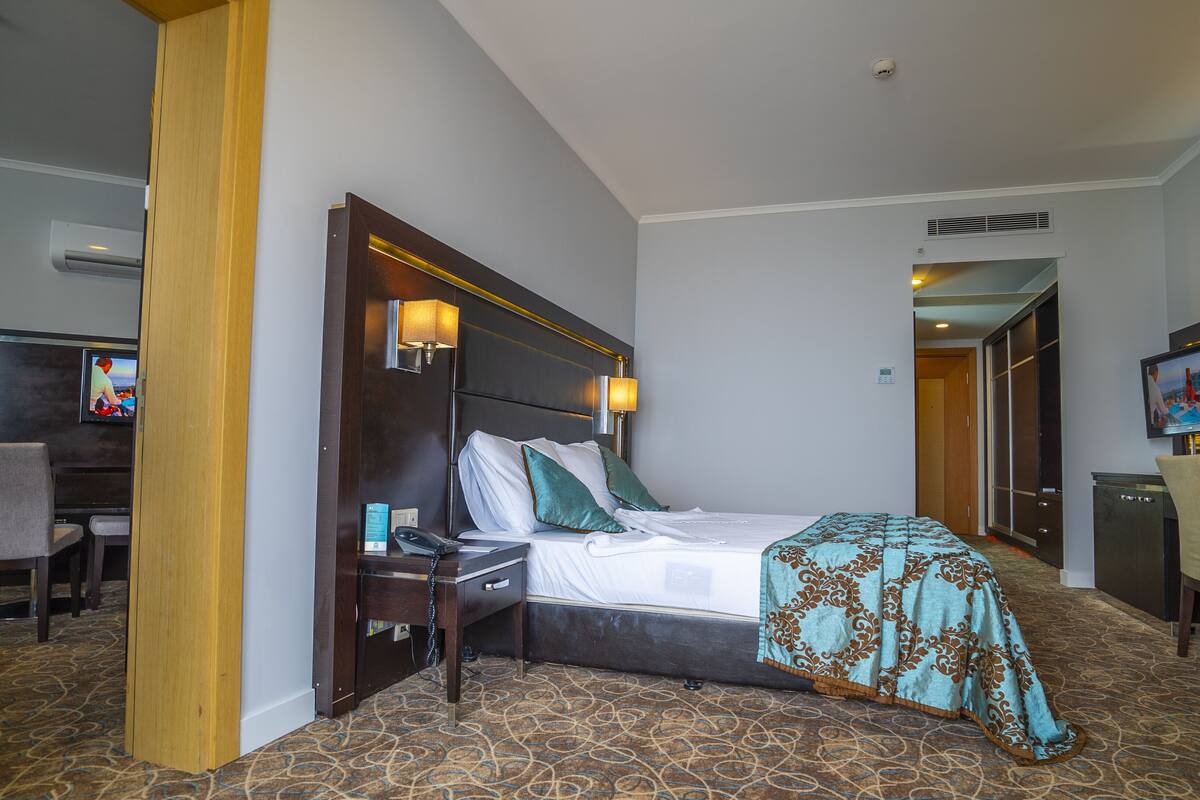 A hotel room with a large bed, bedside tables, a desk, a chair, and a television.