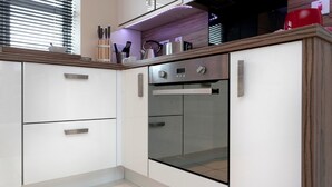 A modern kitchen with white cabinets, a built-in oven, and a glass countertop. - The Coach House (Derby)
