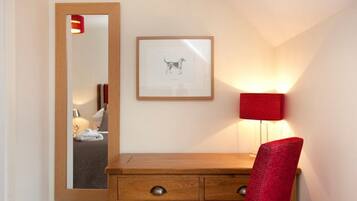 Una camera d'albergo con una scrivania in legno, una sedia rossa, un quadro incorniciato di un cane, uno specchio e una lampada da comodino.