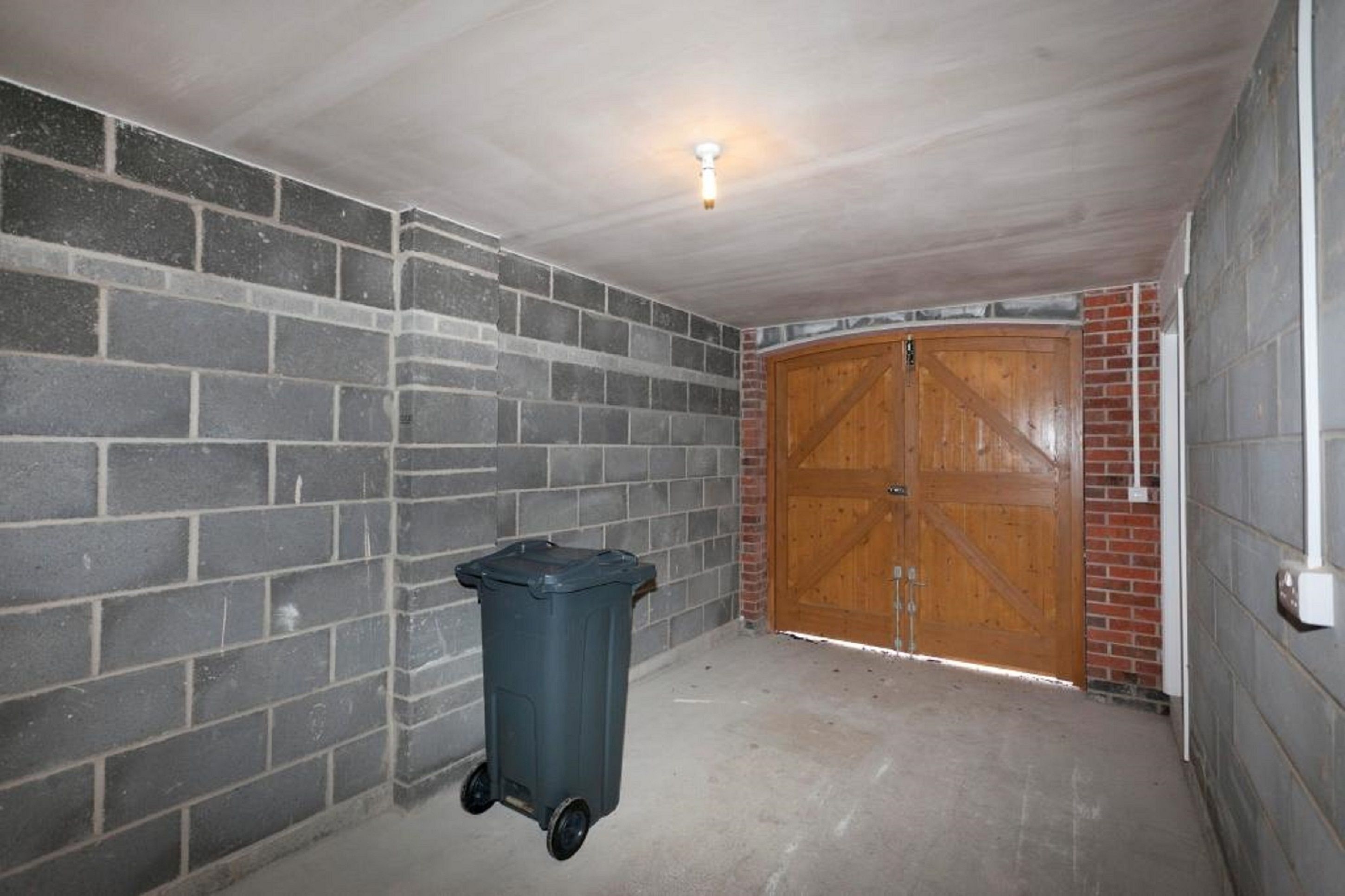 Una habitación con pared de ladrillo, puerta de madera y un bote de basura.
