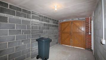 Una habitación con pared de ladrillo, puerta de madera y un bote de basura.