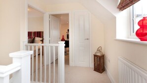 A hallway with a white railing, a door, a window with a red object, and a small table with a lantern. - The Twain (Derby)