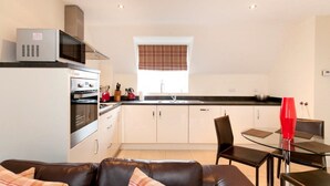 A compact kitchen with modern appliances, a dining area with a glass table, and a cozy seating area with a leather couch. - The Twain (Derby)