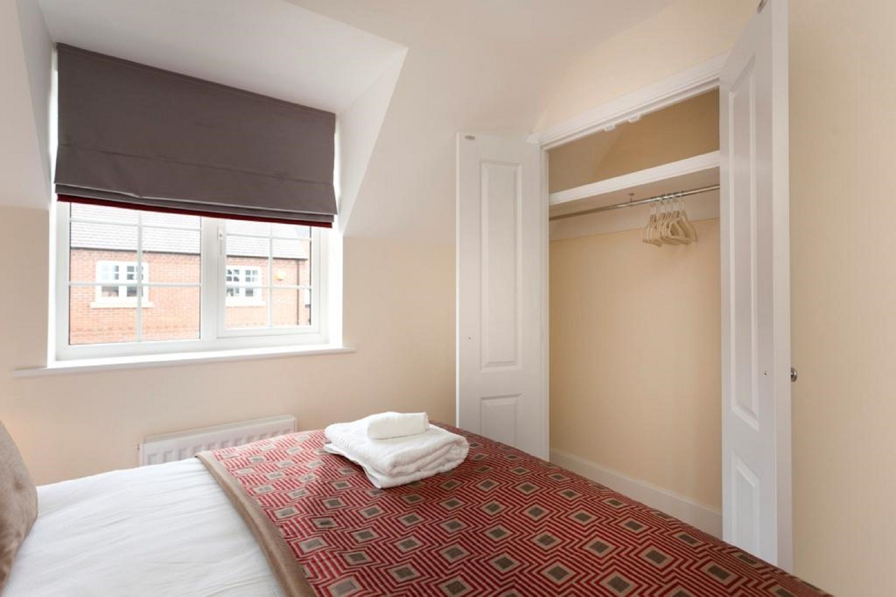 Une chambre à coucher avec un lit, une fenêtre avec un store, une armoire où sont suspendus des vêtements et un radiateur.