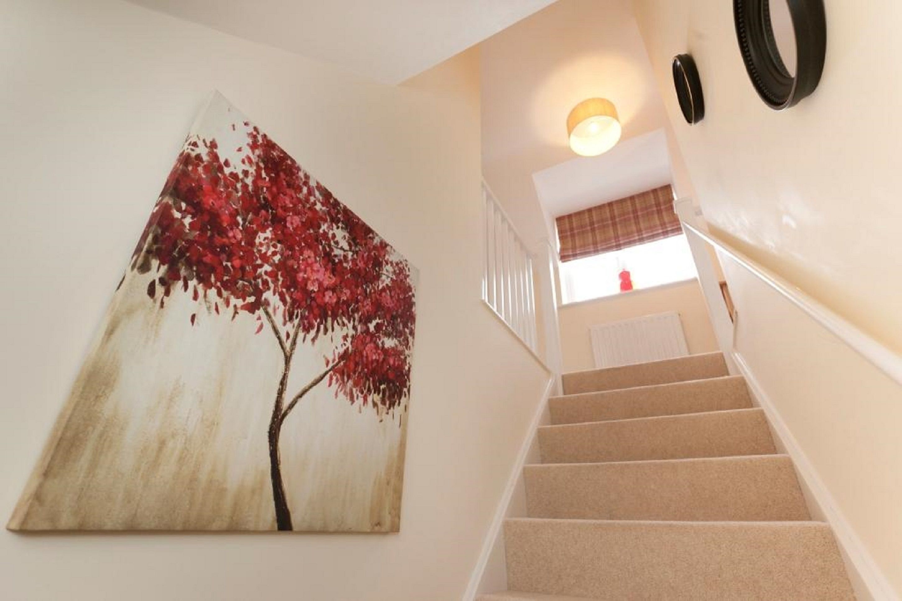 A staircase with beige carpeted steps and a wall-mounted painting of a tree with red leaves.