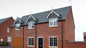 A row of brick houses with pitched roofs, a central garage door, and a small front porch. - The Twain (Derby)