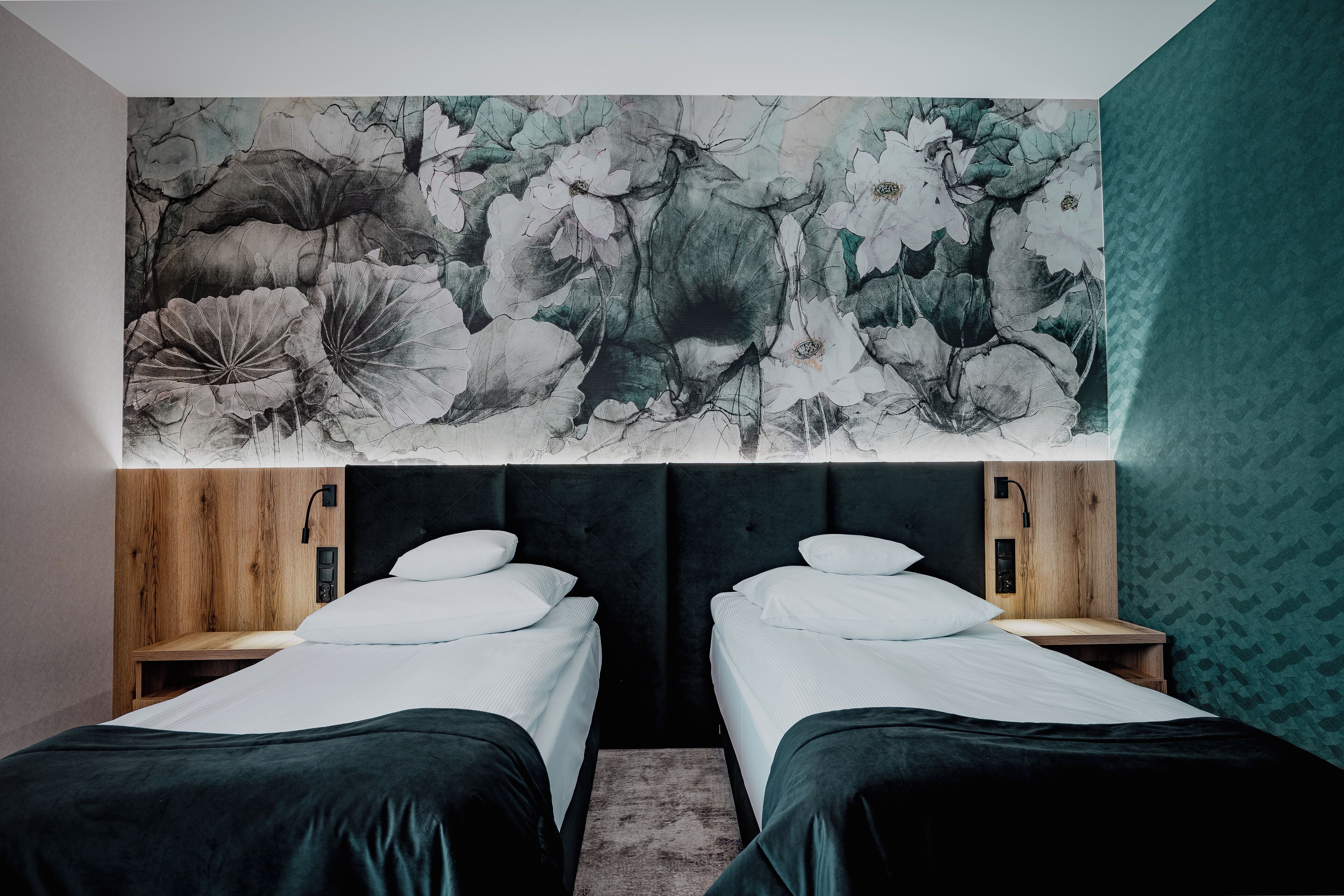 A room with two beds, a large floral mural on the wall, and a wooden headboard.