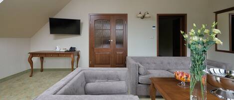 Un salón con un sofá gris, una mesa de centro de madera, un televisor de pantalla plana montado en la pared, una puerta de madera y un jarrón con flores sobre una mesita auxiliar.