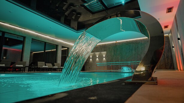 Una piscina interior moderna con un elemento acuático único y zona de descanso.