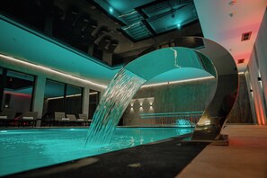 Una piscina interior moderna con un elemento acuático único y zona de descanso.