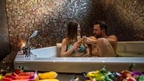 Una pareja en una bañera con pared de mosaicos y flores alrededor.