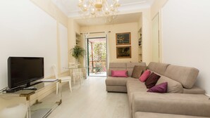 A living room with a flat-screen TV, a beige sofa with multiple cushions, a glass coffee table, and a dining area with chairs and a table. - Rental in Rome Augustus Terrace Deluxe (Rome)
