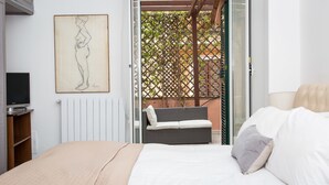 A bedroom with a bed, a television, a painting, and a balcony with a wicker chair. - Rental in Rome Augustus Terrace Deluxe (Rome)