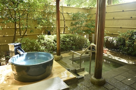 A traditional Japanese onsen with a large stone hot tub, wooden steps, and bamboo walls.