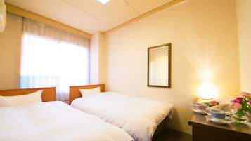 A hotel room with two beds, a bedside table with a lamp, a mirror, and a window with curtains.