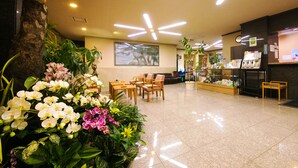A hotel lobby with a reception desk, seating area, and a large plant with orchids. - Hotel Matsukaze (Toyota)