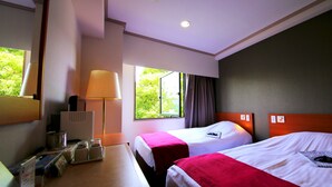 A hotel room with two beds, a desk with a lamp, a window with curtains, and a view of greenery outside. - Hotel Matsukaze (Toyota)