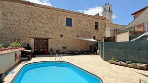 A swimming pool with a ladder, surrounded by a stone building with a tiled roof and a bell tower. - Palacio de Velamazán (Velamazan)
