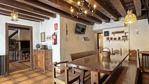A rustic interior with a wooden dining table, benches, a chandelier, a fireplace, and a television mounted on the wall. - Palacio de Velamazán (Velamazan)