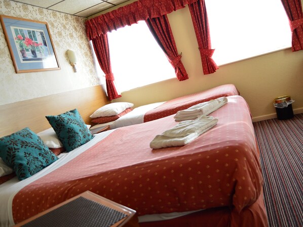 A hotel room with two beds, red curtains, a framed picture on the wall, and a small trash bin.