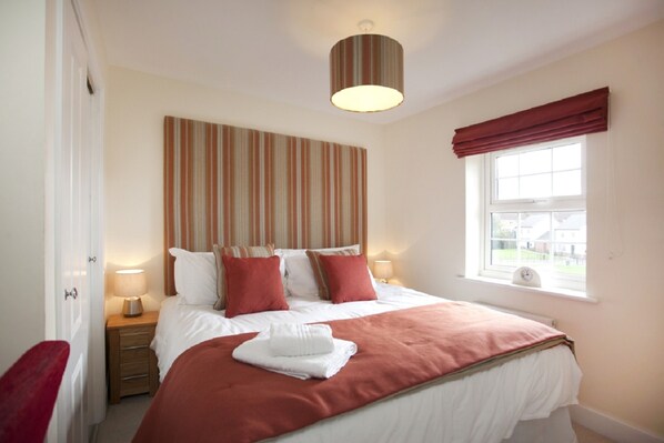 A neatly made bed with pillows, a bedside lamp, and a window with curtains.