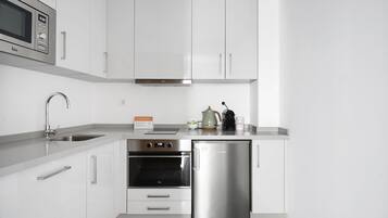 A modern kitchen with white cabinets, stainless steel appliances including a microwave, oven, and refrigerator, a sink, and a countertop with a kettle and coffee maker.