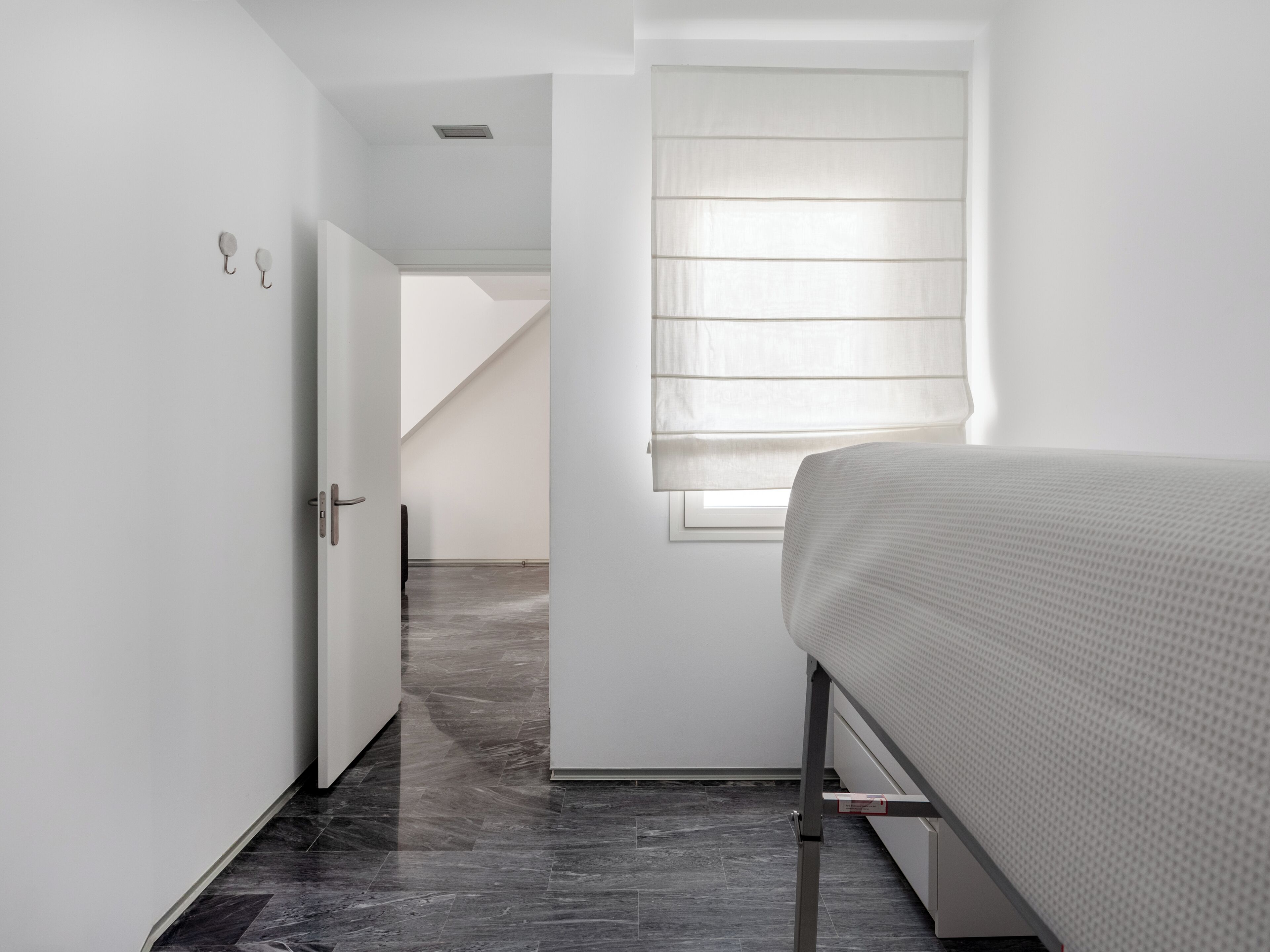 A minimalist bedroom with a bed, a door, and a window with blinds.