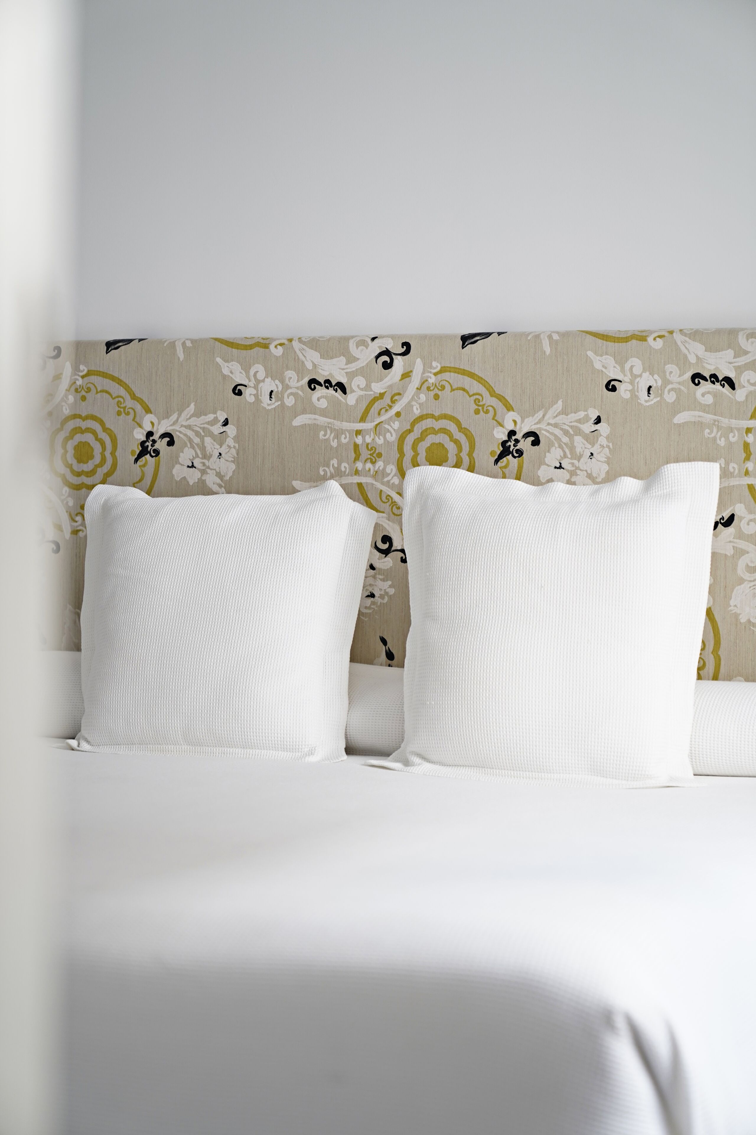 A bed with white bedding and two white pillows against a patterned wallpaper.