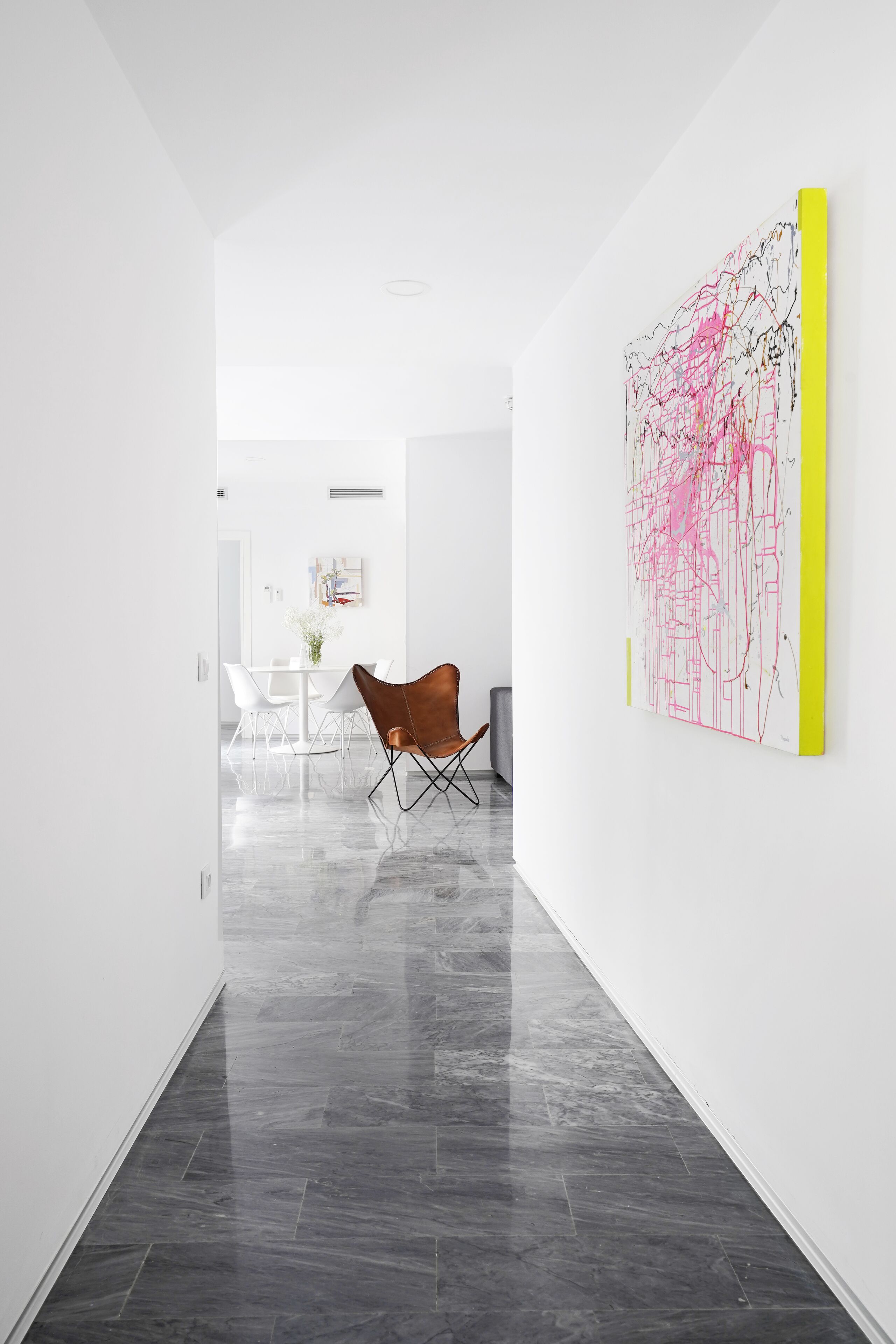 Un interior moderno con una zona de comedor, una silla marrón y un cuadro abstracto grande en la pared.