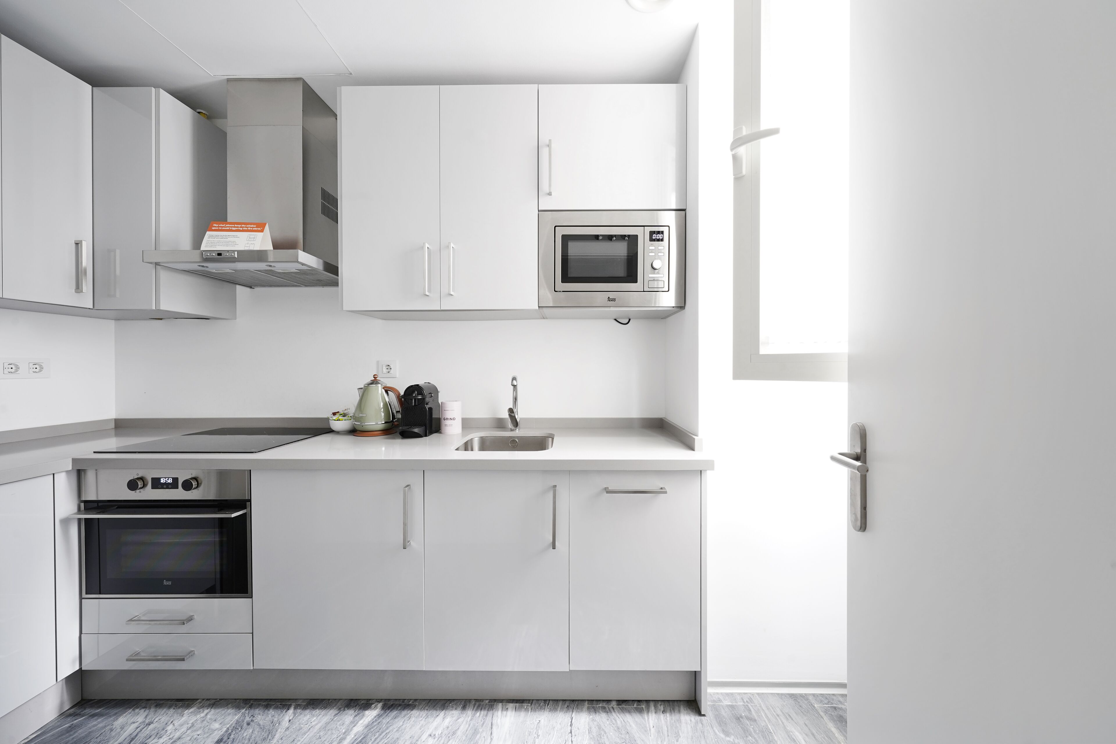 A modern kitchen with white cabinetry, a built-in oven, a microwave, and a stainless steel sink.
