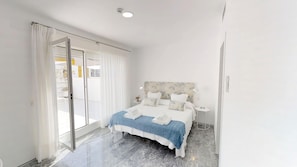 A modern bedroom with a large bed, a sliding glass door to a balcony, and a nightstand with a lamp. - Numa Seville Jondo (Seville)