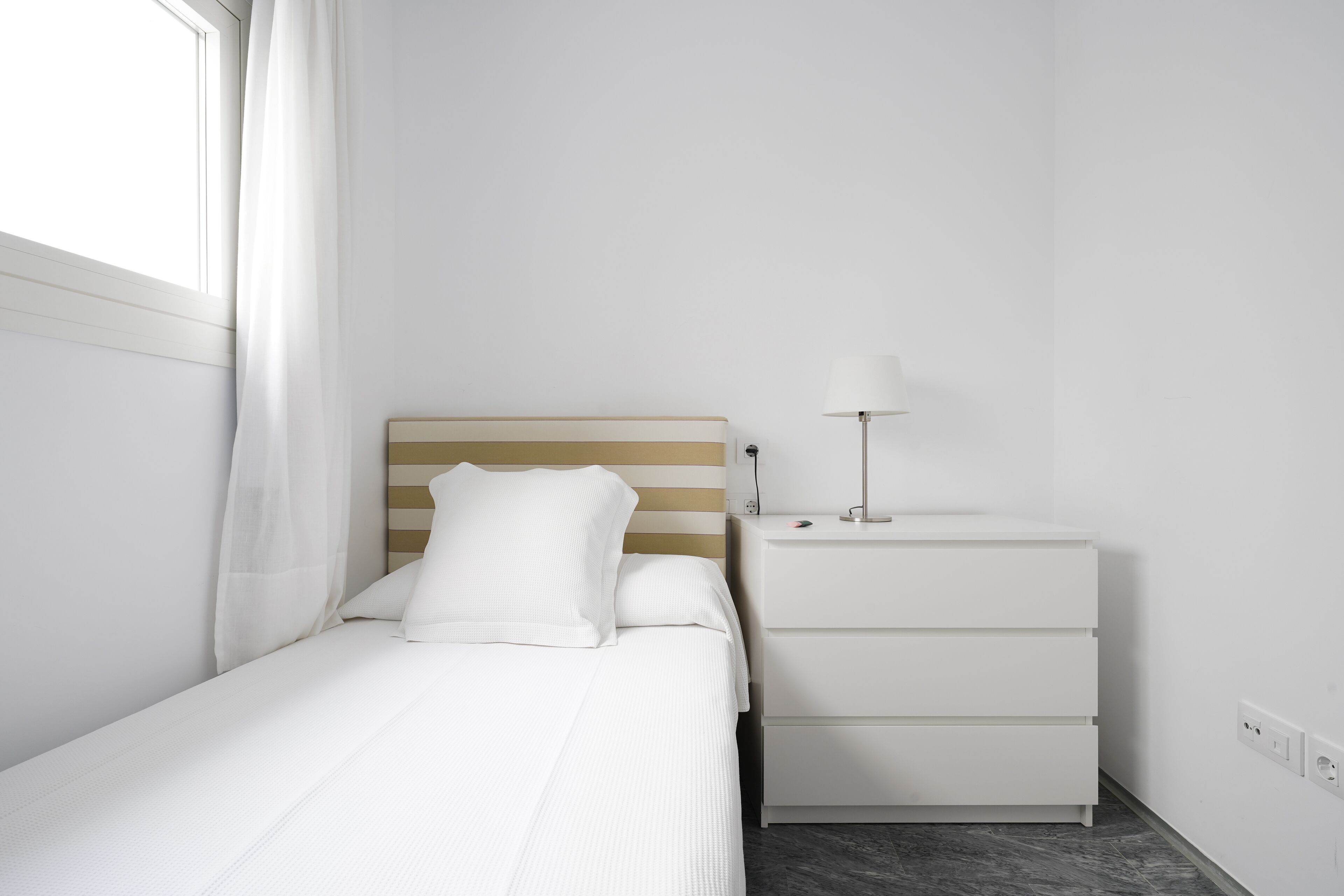 Una stanza piccola e pulita con un letto, un comodino e una lampada.