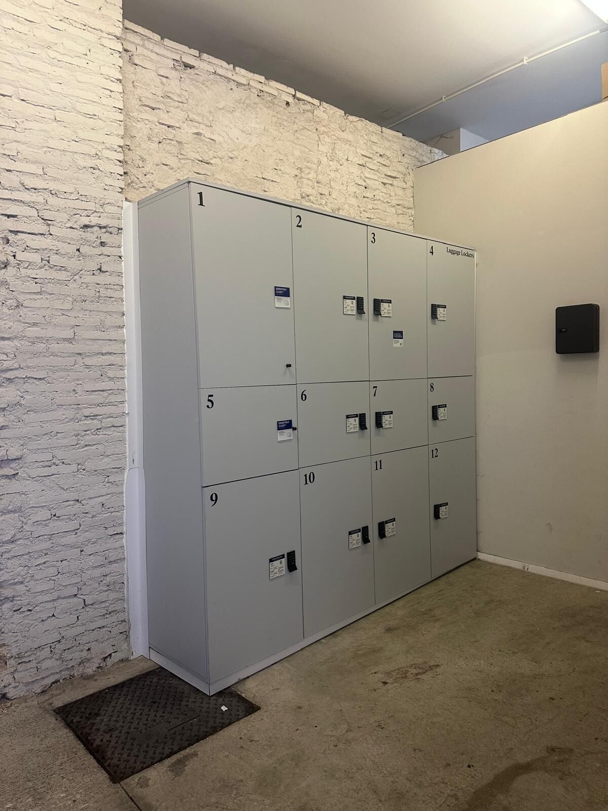 A row of grey lockers with numbers, a white brick wall, and a carpeted floor.
