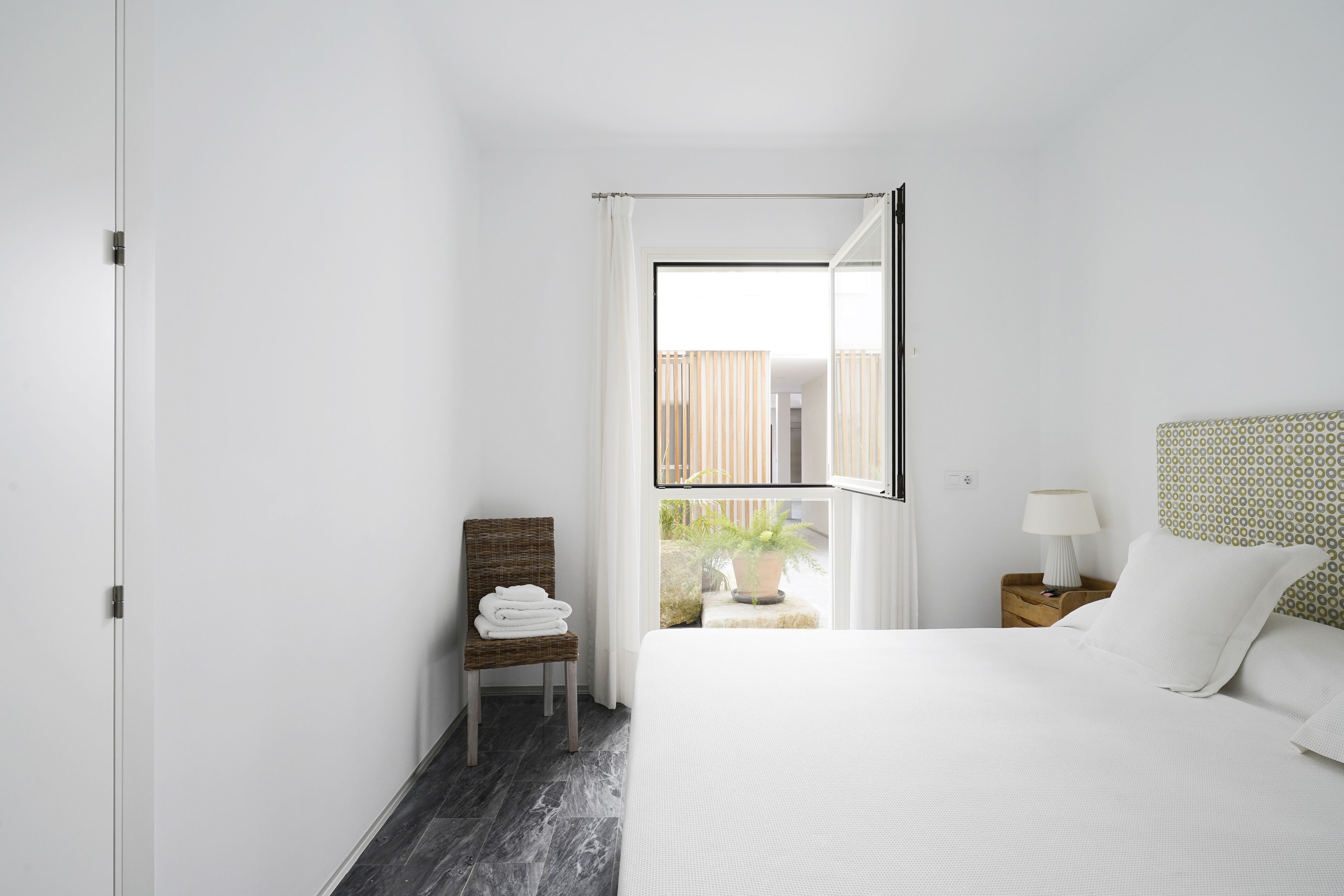A hotel room with a bed, a chair, a nightstand, a lamp, and a window with curtains.