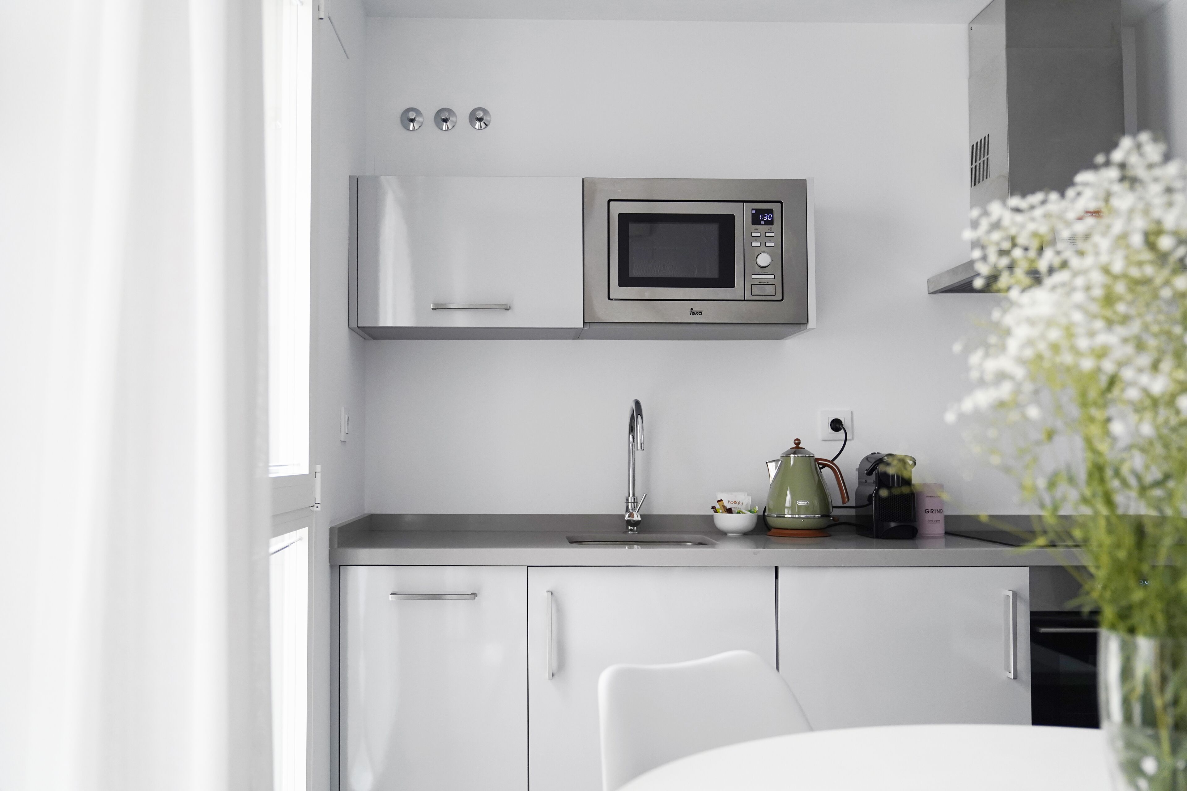 A modern kitchen with white cabinets, a stainless steel microwave, a sink, and a kettle.
