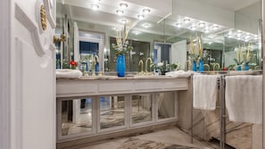 A modern bathroom with a large mirror, gold faucets, and a marble countertop.