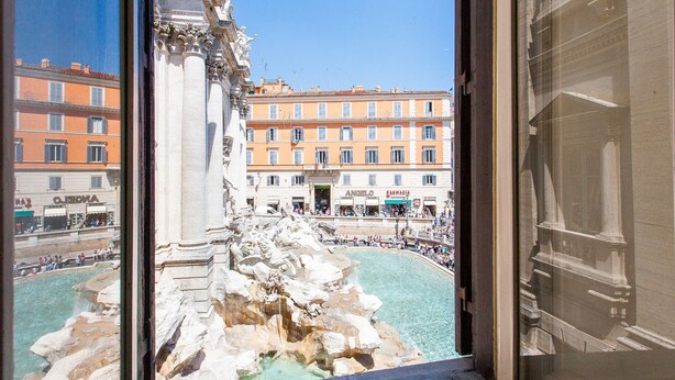 A view of the Trevi Fountain from inside a building, with the Baroque architecture of the surrounding buildings and the fountain's intricate details visible. - Rental in Rome Crociferi 1 (Rome)